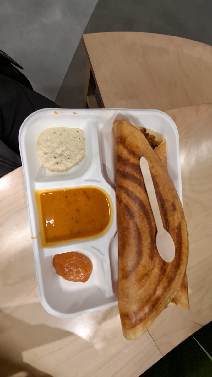 A crisp folded dosa with coconut chutney, sambar and tomato chutney in a takeaway tray