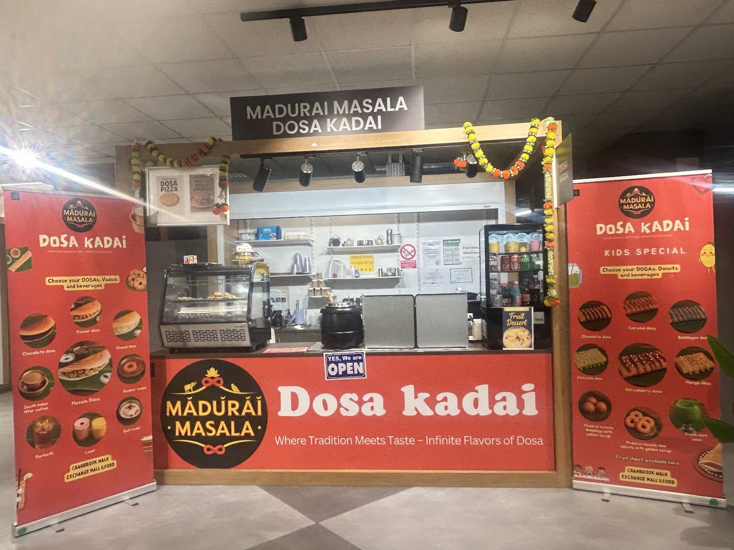The Madurai Masala Dosa Kadai stall front with red branding and marigold garlands inside The Exchange, Ilford